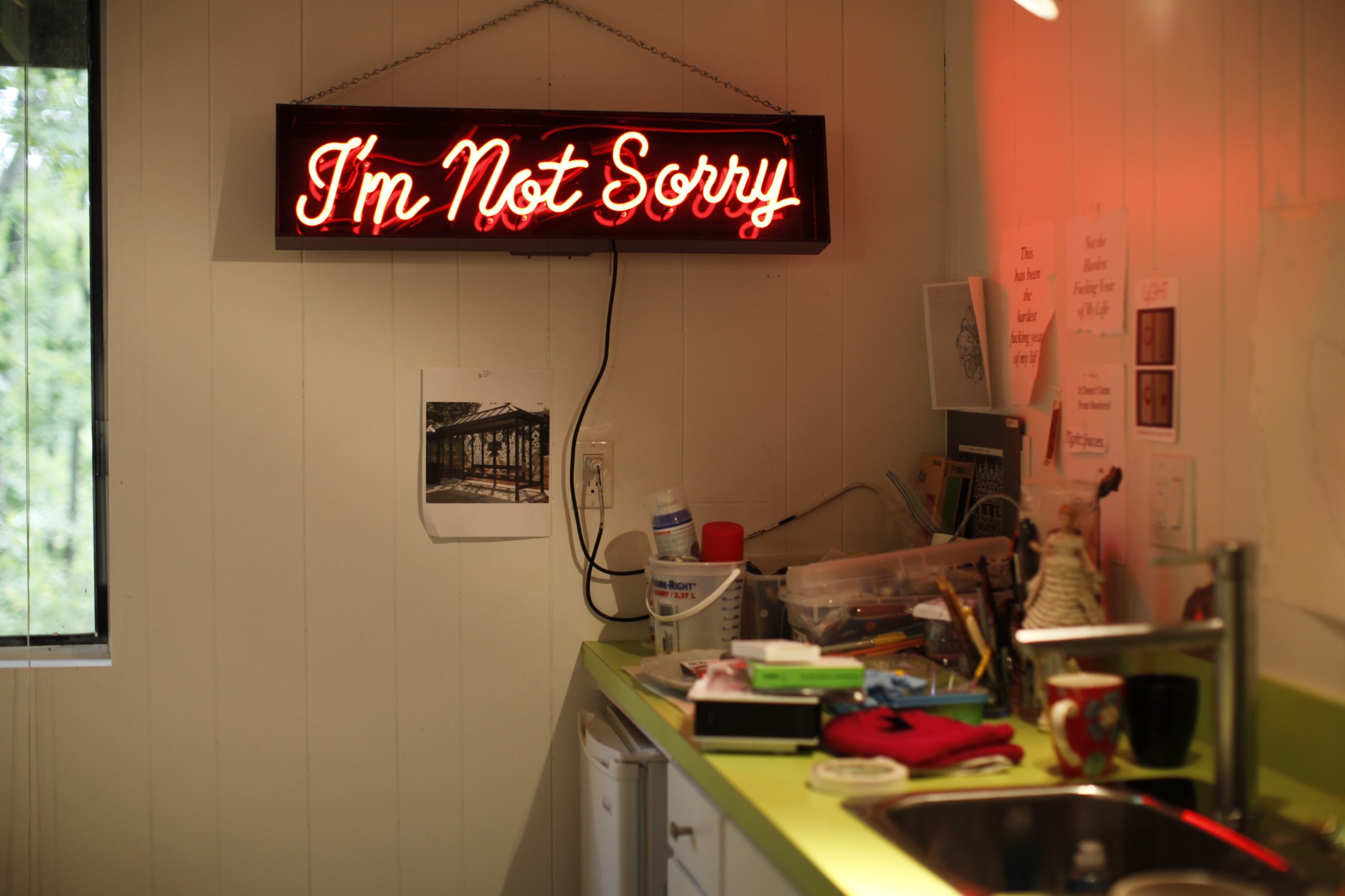 Photograph of Susan Harbage Page's studio with mess on a countertop and a neon sign that says "I'm Not Sorry"